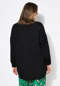 Camicia nera con bottoni, realizzata in tessuto texturizzato, spalle a caduta e maniche lunghe, abbinata a pantaloni verdi stampati con macchie di leopardo.