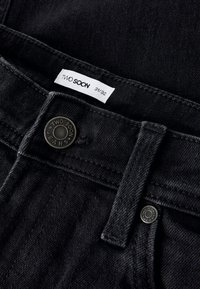 Pantalones vaqueros negros de denim con un acabado texturizado. Presentan un botón metálico con la marca y una etiqueta de cuidado que indica la talla 31/32.
