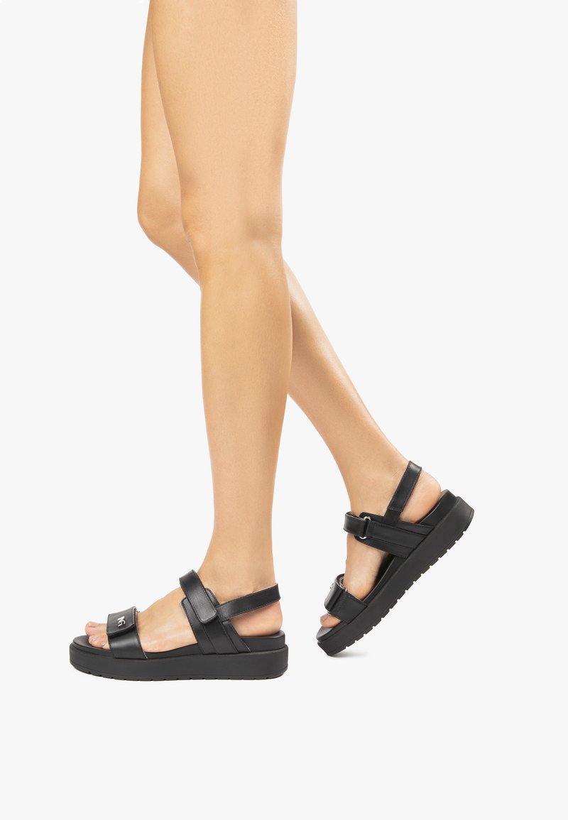 Sandali platform neri con design ampio e a strisce. Realizzati in materiale sintetico liscio, presentano una fibbia regolabile per una vestibilità sicura.