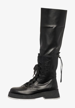 Botte en cuir noir jusqu'au genou avec une semelle texturée, un devant à lacets et une partie supérieure lisse. Détail de fermeture éclair sur le côté.