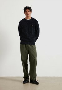 Suéter de punto azul marino con motas, textura acanalada, cuello redondo; combinado con pantalones sueltos de color verde oliva y zapatos negros con suelas gruesas.