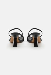 Sapatos de salto em verniz preto com um salto quadrado, trás aberto e finas correias para o tornozelo. Textura suave e design versátil para várias ocasiões.