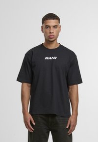 Black cotton t-shirt with a crew neck, short sleeves, and white "KANU" text logo on the chest. Relaxed fit and smooth texture.