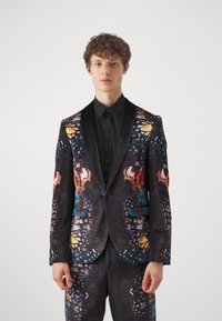Tailored suit with a black base, featuring a colorful butterfly pattern. The jacket has a satin shawl collar and two front pockets.