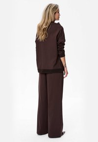 Brązowa, oversize'owa bluza i dopasowane spodnie z szerokimi nogawkami, wykonane z miękkiego materiału, z prążkowanymi mankietami i dołem. Minimalistyczny i swobodny design.