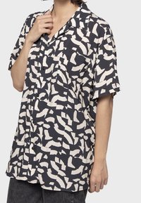 Camicia a maniche corte di un blu navy scuro con motivi astratti bianchi. Presenta un colletto e una tasca sul petto. Tessuto morbido e leggero.
