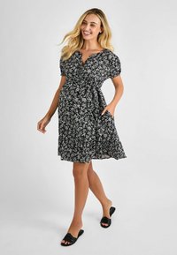 Abito nero floreale con maniche a sbuffo corte, scollatura a V e tasche. Realizzato in tessuto leggero con vita legata, presenta piccoli fiori bianchi.