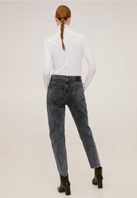 Černé vysoké džíny s vybledlým odstínem, které mají dvě zadní kapsy, v kombinaci s upnutým bílým topem s dlouhým rukávem a hnědými botami na podpatku.