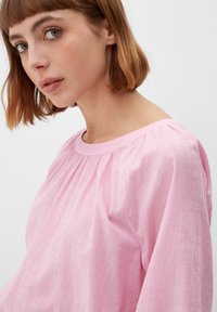 Roze gestreepte blouse met een ronde hals, geplooid ontwerp en losse pasvorm. De stof lijkt zacht met een lichte textuur en ontspannen mouwen.
