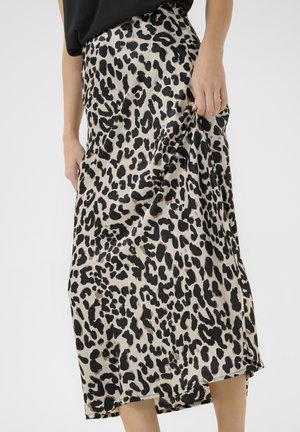 Naine kannab beeži ja musta leopardimustriga midi seelikut, hoides kangast ühel küljel, must top on vöökohas nähtav.