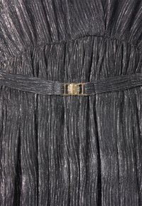 Gros plan d'une robe en tissu plissé noir brillant avec une fine ceinture assortie comportant une petite boucle dorée à la taille.