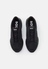 Zapatillas deportivas negras con un upper de tela texturizada, prominente logotipo "BOSS" en la lengüeta y suela de goma. Diseño minimalista con una marca sutil.