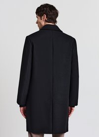 Soprabito nero in misto lana con colletto a rever, taglio dritto e maniche lunghe. Presenta un design posteriore senza cuciture e dettagli minimi.