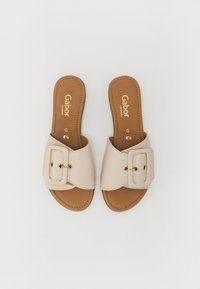 Sandali a ciabatta beige con una larga fascia decorata da una fibbia e hardware dorato su una soletta marrone, progettati per il massimo comfort.