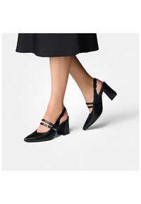 Talons escarpins en cuir noir avec des pointes en amande, des talons carrés et épais, et deux brides horizontales ornées de boucle en métal.