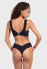 Čierny plavkový set, ktorý obsahuje braletku so širokými ramienkami a výstrihom do tvaru V na chrbte. Spodná časť plaviek má nízky strih a dizajn prednej časti do tvaru V.