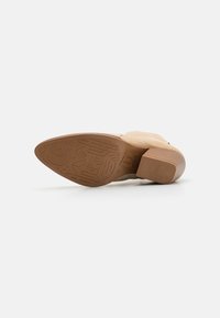 Botín de ante beige con tacón bloque, suela de goma con un patrón de agarre texturizado y diseño de punta redonda.