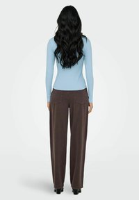 Jasnoniebieska, prążkowana bluzka z długim rękawem, zestawiona z brązowymi, luźnymi spodniami z wysokim stanem. Czarny obcas dopełnia całość stroju.
