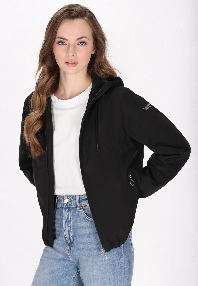 Kvinnors svart zip-up jacka med huva, med en frampocket, lätt tyg och elastiska ärmmuddar. Bärs över en vit skjorta.