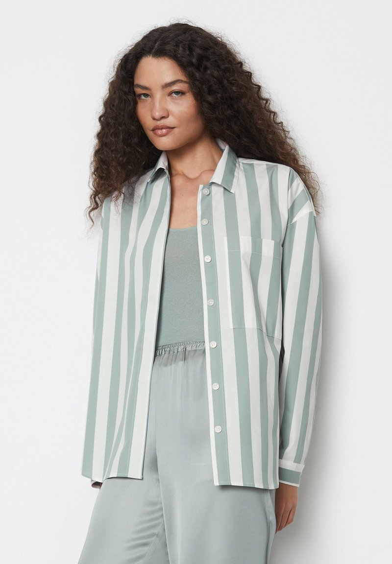 Camicia a righe verde chiaro e bianca con scollo a collare, tasca sul petto e vestibilità comoda, indossata sopra un top verde uniforme.