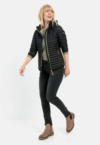 Sort pufferjakke med hætte, letvægts, lynlåslukning, sidelommer; parret med olivengrøn trøje og sorte jeans, lysebrune ankelstøvler.