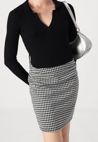 Svart ribbad långärmad topp med v-ringning, i kombination med en minikjol i hundtandsmönster i svart och vitt. Silverfärgad handväska som accent.