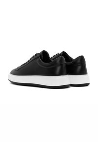 Baskets en cuir noir avec une semelle en caoutchouc blanc, présentant un design minimaliste, une forme arrondie, et un système de laçage noir.