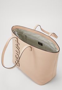 Beige leren tote bag met dubbele banden, "Hugo" logo aan de zijkant, en een ritsvak aan de binnenkant met een lichte voering.