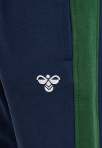 Marina joggers med ett grönt sidostreck, med en vit bi-logotyp på låret. Gjorda av mjukt, texturerat tyg.