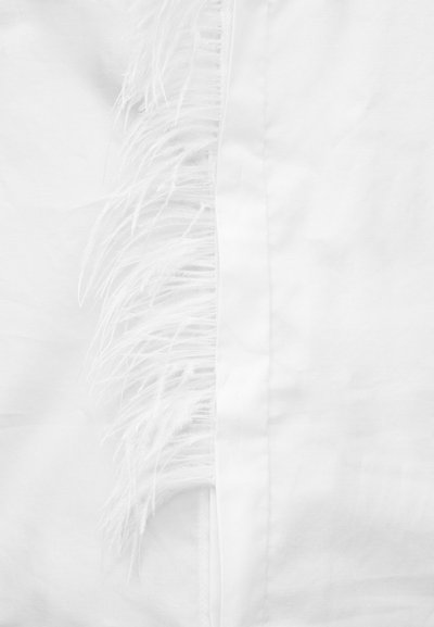 Λευκό ύφασμα με κεντρική ραφή και λεπτές, απαλές φτερωτές φούντες που εκτείνονται από τη μία πλευρά της ραφής.