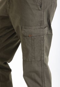 Pantalons cargo en coton vert olive, avec des poches latérales, des coutures visibles et une petite étiquette de marque sur la poche.