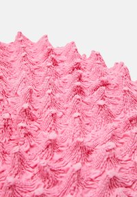 Tessuto rosa testurizzato con un design a motivi che presenta forme zigzag rialzate e piccoli dettagli arrotondati su tutta la superficie.