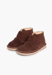 Botas de tobillo de ante marrón con una correa de velcro, costuras beige y una suela marrón claro. Textura suave y forma redondeada para mayor comodidad.