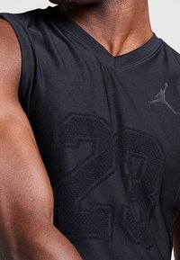Černé sportovní tílko bez rukávů s jemným texturovaným designem "23", V-krkem a logem Jordan na levé horní straně.