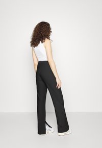 Svarta skräddarsydda byxor med hög midja, vida ben, slitsar på sidorna vid botten, kombinerat med en vit linne och sneakers.