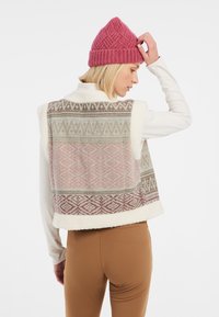 Stickad väst i krämfärg med pastellfärgade geometriska mönster. Har en fluffig textur och en vit fleecefoder. Matchad med en rosa stickad mössa.