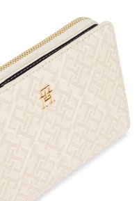 Μπεζ πορτοφόλι με υφασμένο γεωμετρικό μοτίβο, χρυσά μεταλλικά στοιχεία και φερμουάρ. Διακριτική ανάγλυφη λεπτομέρεια με το λογότυπο στην πρόσοψη.