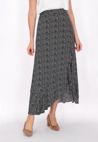 Maxi-jurk in zwart met een wit bloemenpatroon, voorzien van een rucheszoom en een asymmetrisch ontwerp. Draag het met tan blokhakken.