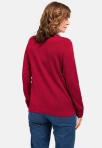 Roter gestrickter Pullover mit gerippten Bündchen und Saum, mit einem runden Halsauschnitt und einem lockeren Schnitt, getragen zu blauen Jeans.