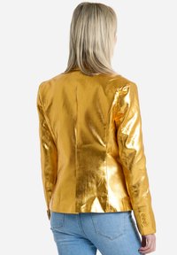 Blazer metálico dorado con hombros estructurados, diseño ajustado y acento de botón en las mangas. Textura suave, costura trasera entallada y silueta moderna.