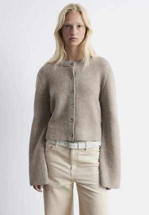 Beige, gestrickte Strickjacke mit Rundhalsausschnitt, Knopfleiste vorne und gerippten Manschetten. Kombiniert mit cremefarbener Cordhose.