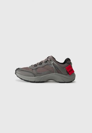 Gray athletic shoes with mesh upper, black accents, and red heel tab. Features laces and textured sole for traction. Modern design.
