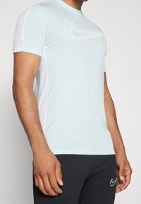Light blue athletic shirt with short sleeves, featuring mesh side panels and a white Nike logo on the front. Smooth texture and fitted design.