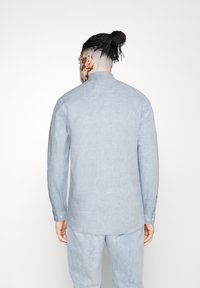 Lichtblauw langemouw shirt met een opstaande kraag, gemaakt van textuurstof. Heeft een rechte snit en knoopmanchetten. Draagt met bijpassende lichte broek.