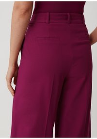 Pantalon magenta avec une coupe ajustée, présentant des poches arrière et une texture lisse. La taille est structurée et se situe au-dessus des hanches.