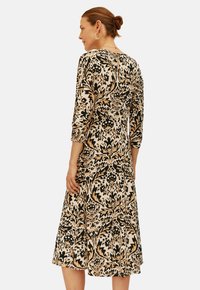 Abito a metà lunghezza con motivo floreale in beige, nero e marrone, con maniche a tre quarti e silhouette svasata. Presenta una chiusura sul retro.