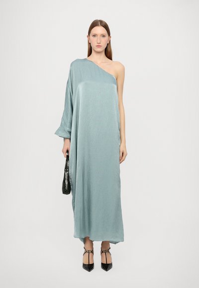 Vestido largo de un solo hombro en tela texturizada de color azul claro. Combinado con un bolso negro y tacones de punta negra.