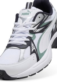 Scarpa sportiva bianca con materiali in rete e sintetici, dettagli neri e verde menta, rifiniture argentate e una spessa suola in gomma.