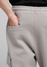 Pantaloni jogger grigio chiaro realizzati in tessuto morbido, con cintura elastica, tasche laterali e cuciture dettagliate. Design casual con utilità pratica.