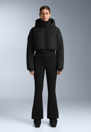 Čierna skrátená puffová bunda s vysokým golierom a predným zipsom, skombinovaná s priliehavými čiernymi rozšírenými nohavicami a lesklými čiernymi platformami.